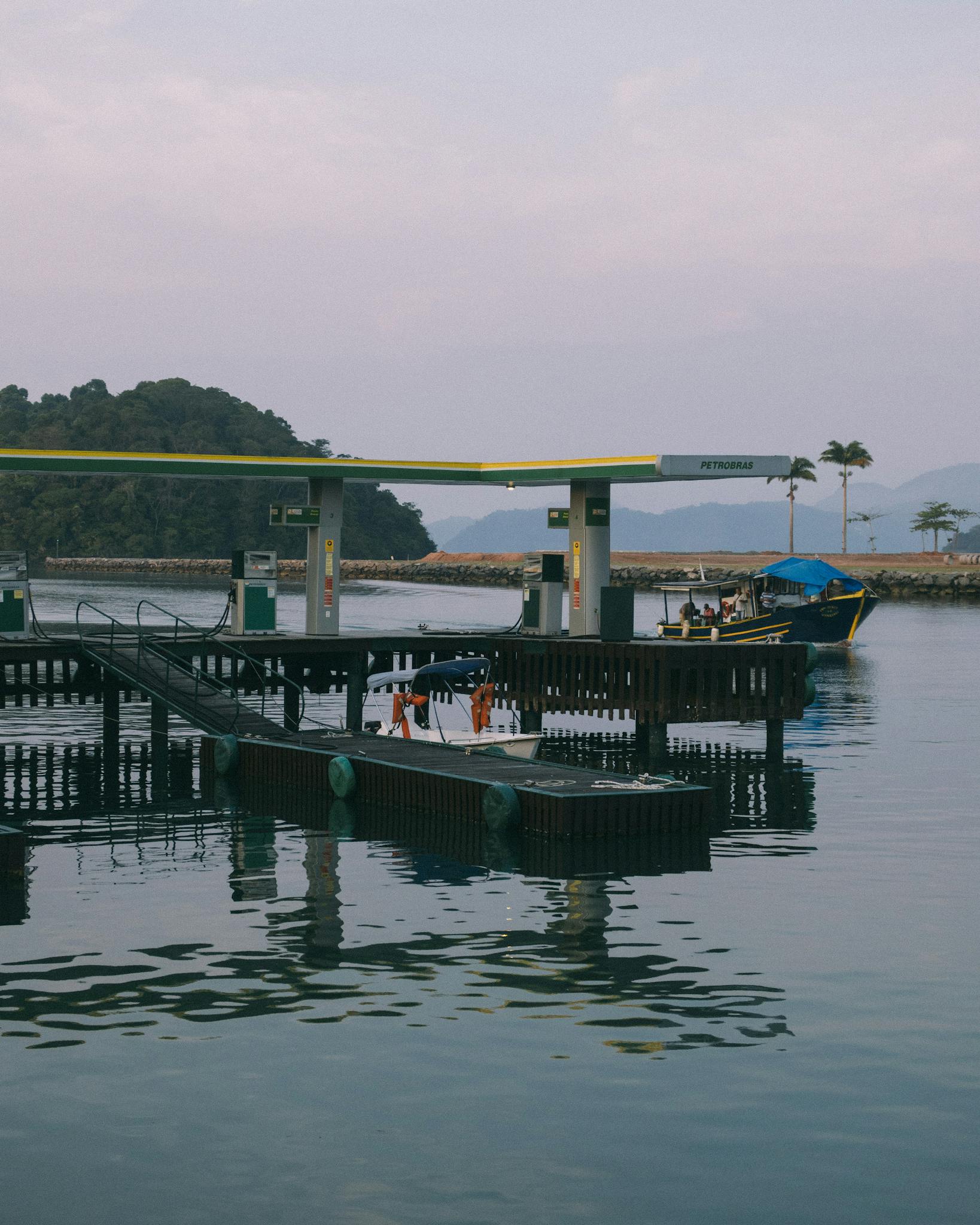 Gas station located on wooden wharf near calm sea against cloudy sky with green mountain on background in summertime outside